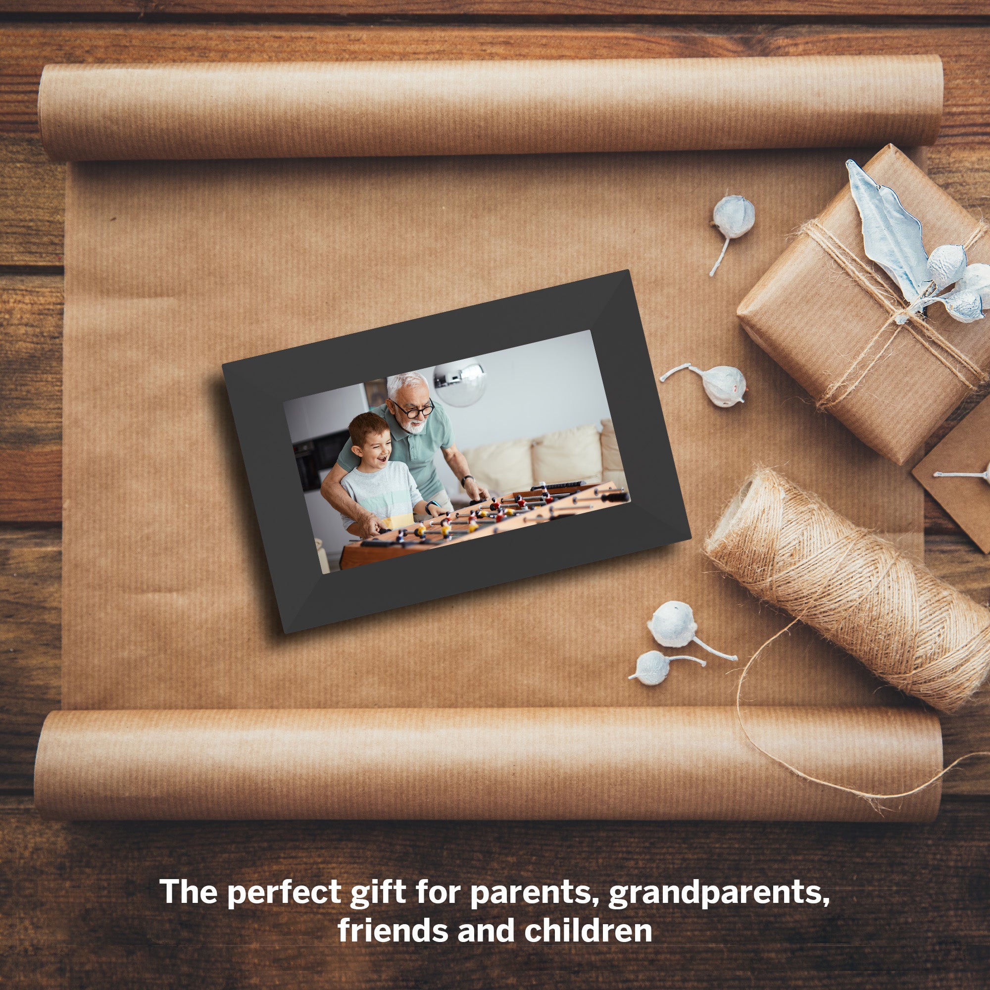 Digital photo frame on brown paper with wrapped gift and decorative elements on a wooden surface